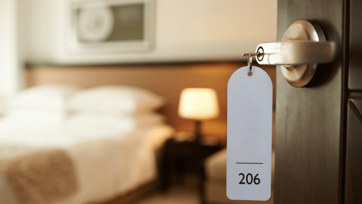 lighting in hotels: hotel room door with a key inside and bedside table lamp