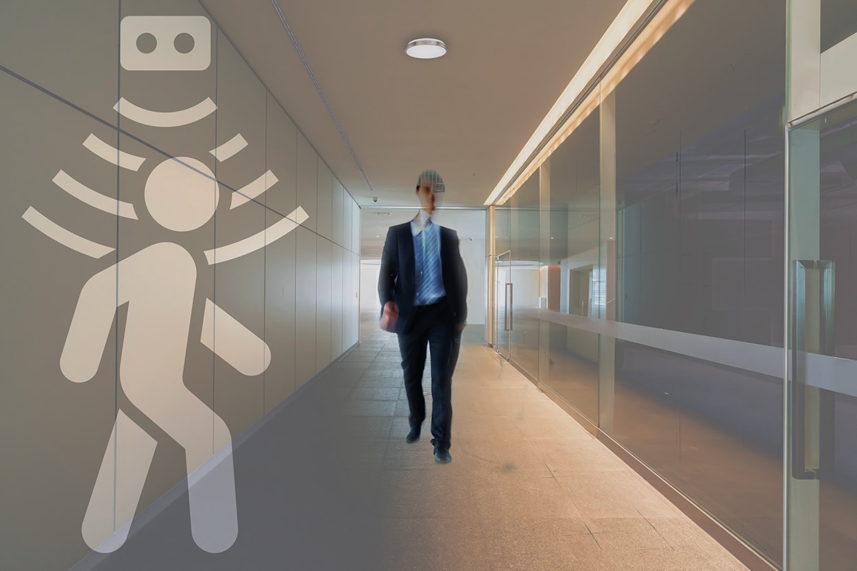 post-pandemic office lighting in a building corridor where a worker if walking and the motion sensor of the ceiling light get activated